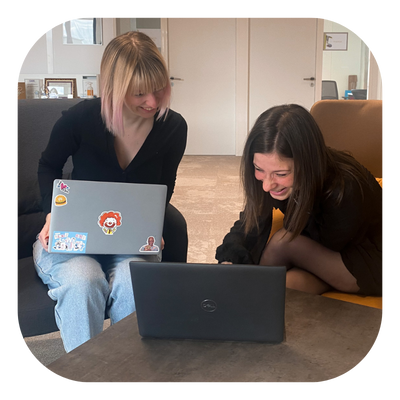 Photo_assistantes_de_vente Deux collaboratrices échangent avec le sourire autour de leurs ordinateurs."